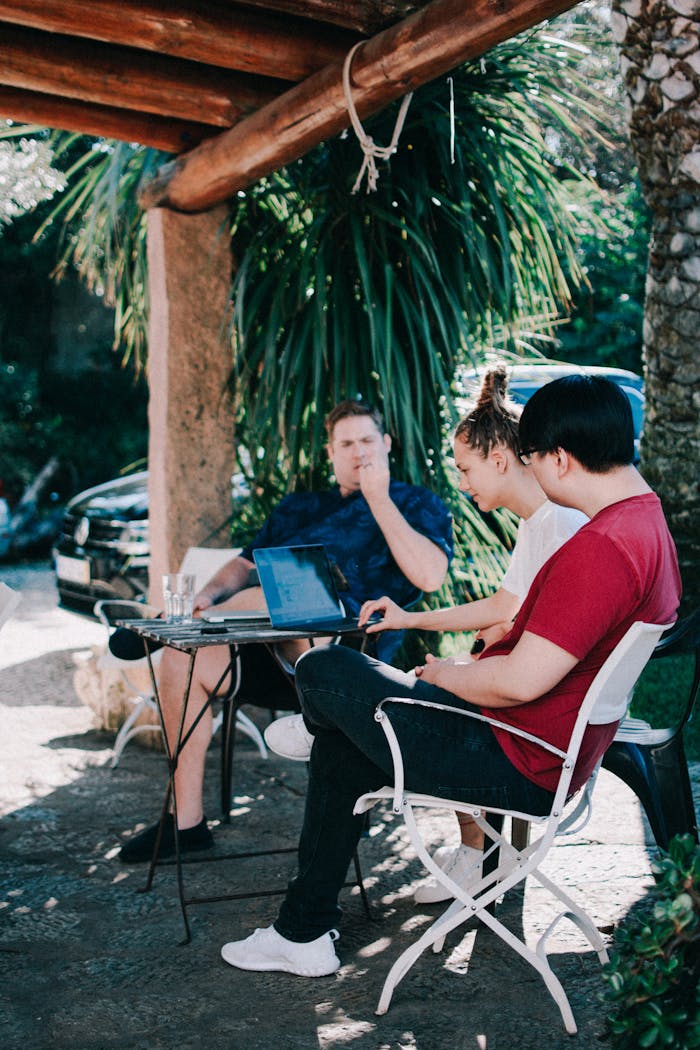 Three adults collaborating outdoors with laptops in a tropical setting.